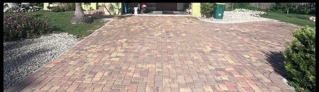 Before: a red paver driveway faded and patchy with tire scuffing, in Bonita Springs, FL — Gulf Coast Sealing & Pressure Cleaning