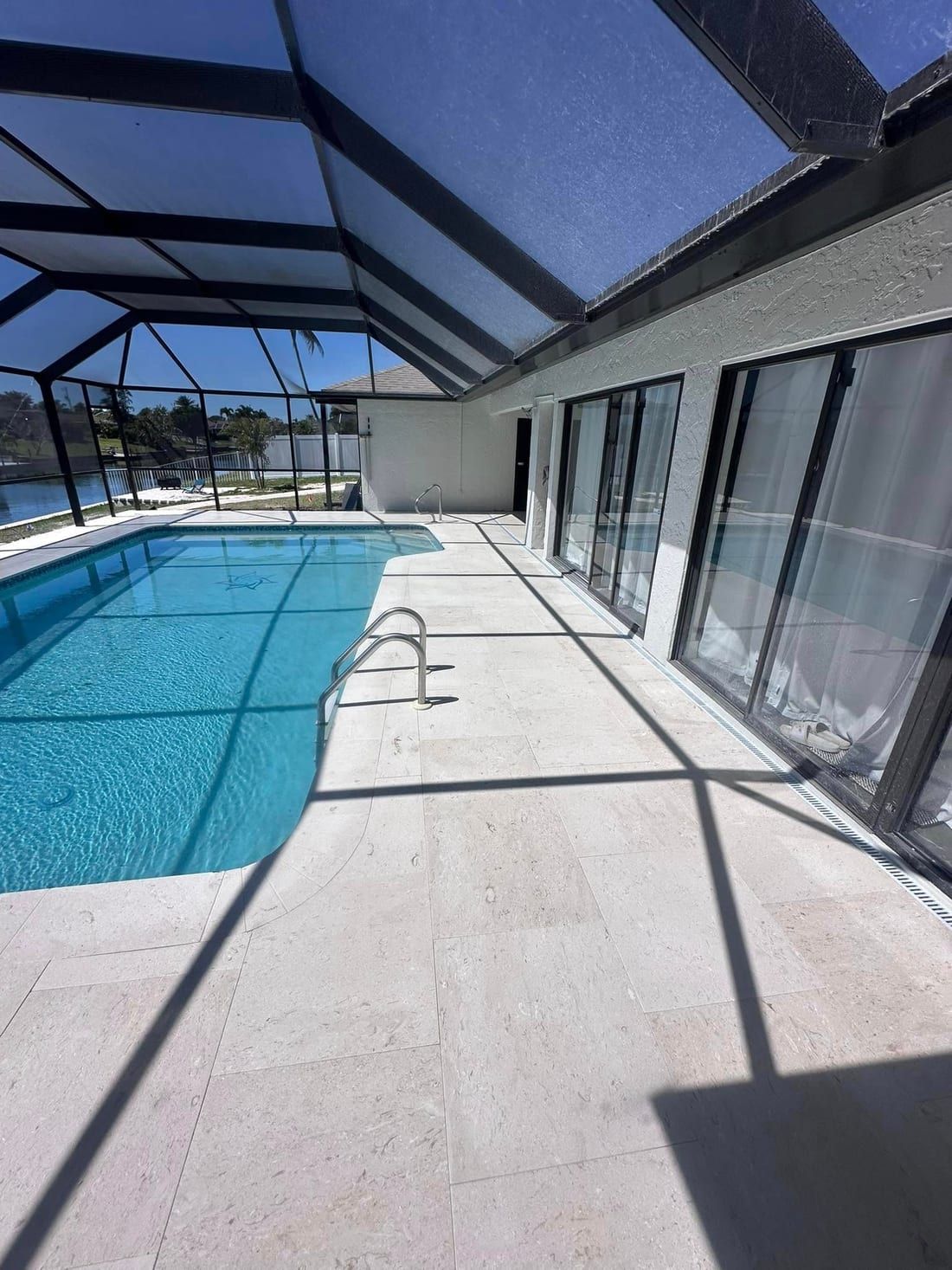 After: the same pool deck and lanai rebuilt in new travertine, with the lake behind, in Southwest Florida — Gulf Coast Sealing & Pressure Cleaning